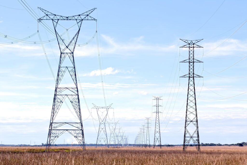High voltage pylons stretching across a vast open field under a clear blue sky