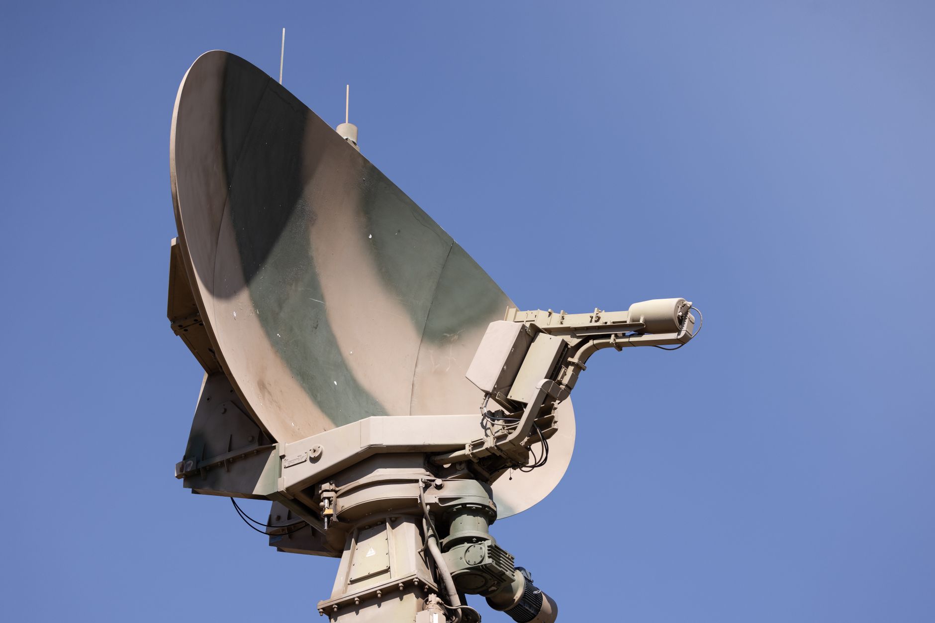 Close-up of a military radar system against a clear blue sky
