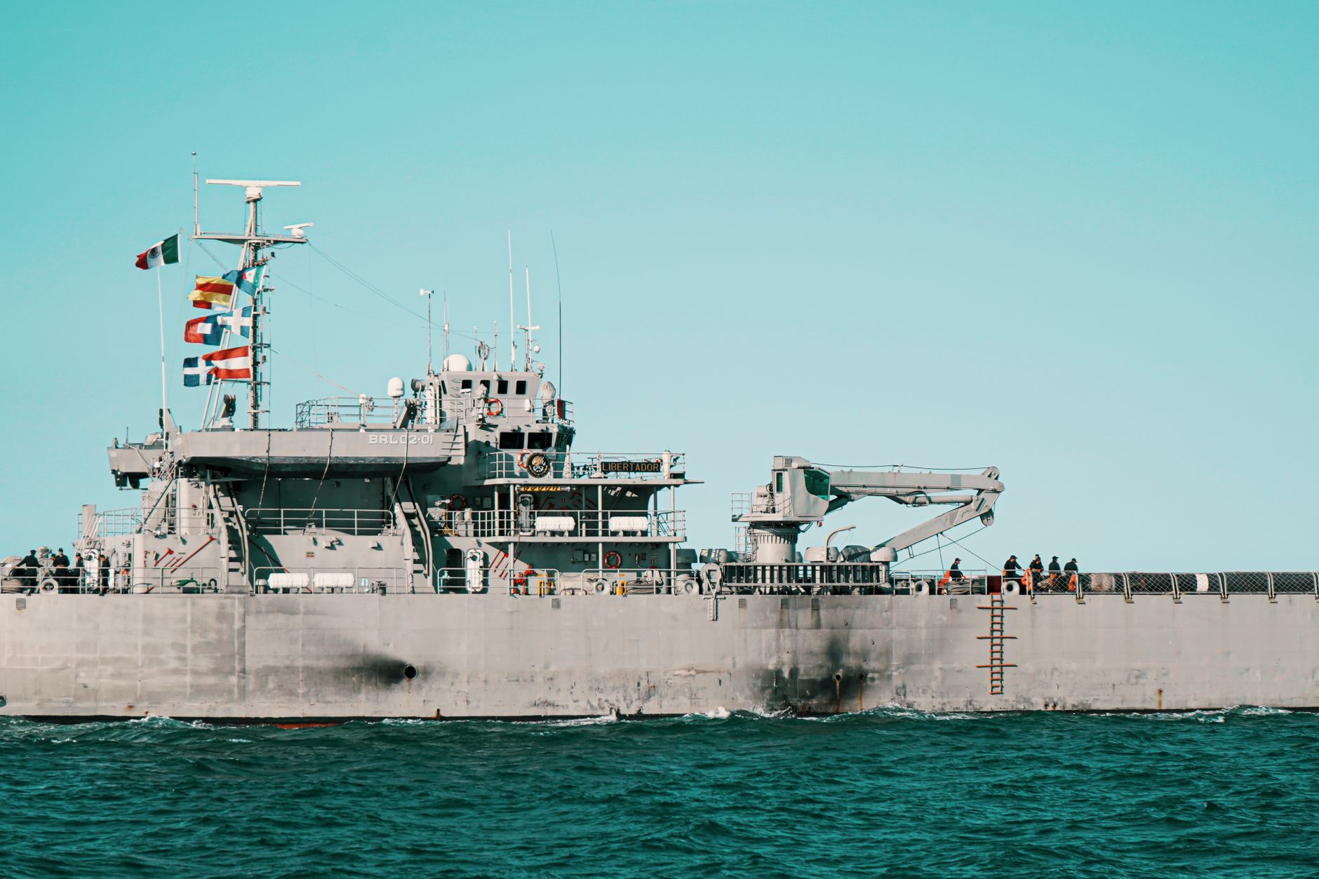 A navy warship sailing in the ocean with flags flying high