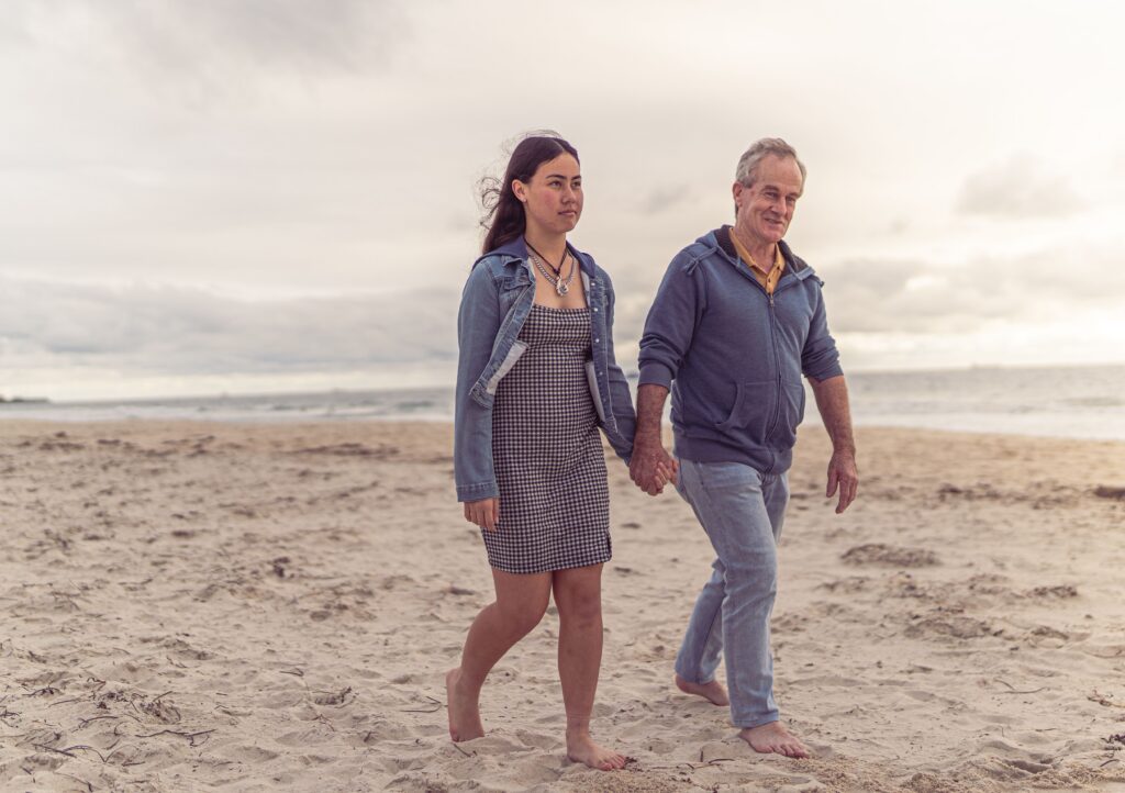 A father and daughter holding hands as they walk barefoot along a sandy beach