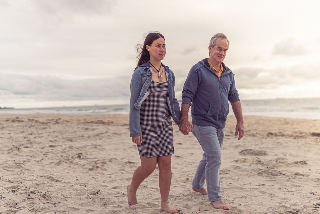A father and daughter holding hands as they walk barefoot along a sandy beach