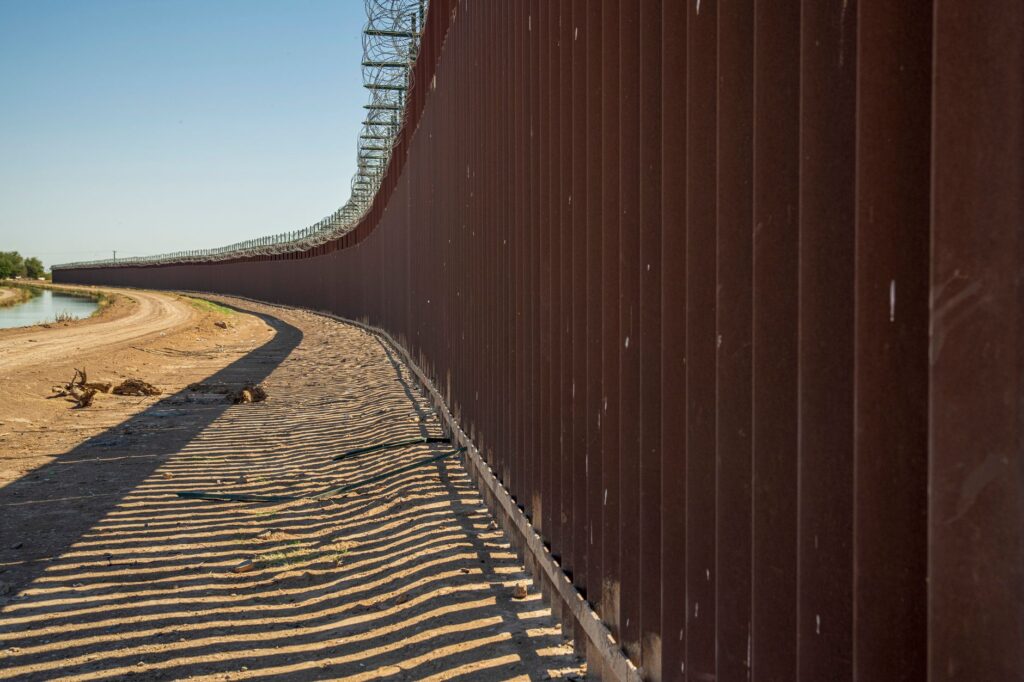 A steel border wall under clear skies