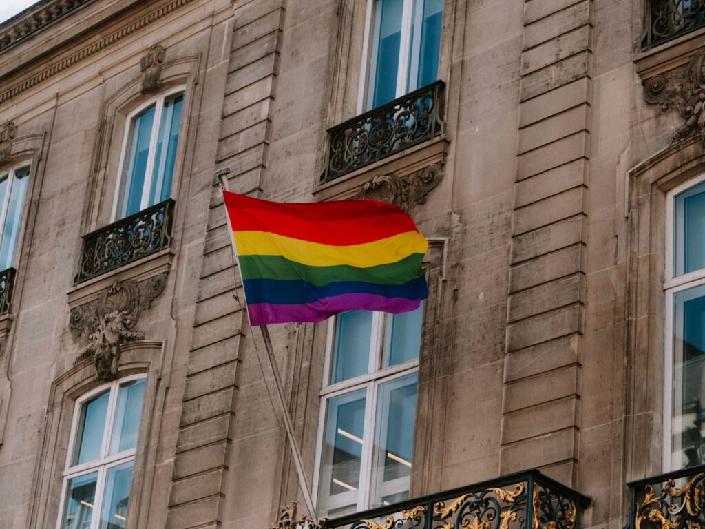 A colorful LGBT pride flag waving in front of a historic building