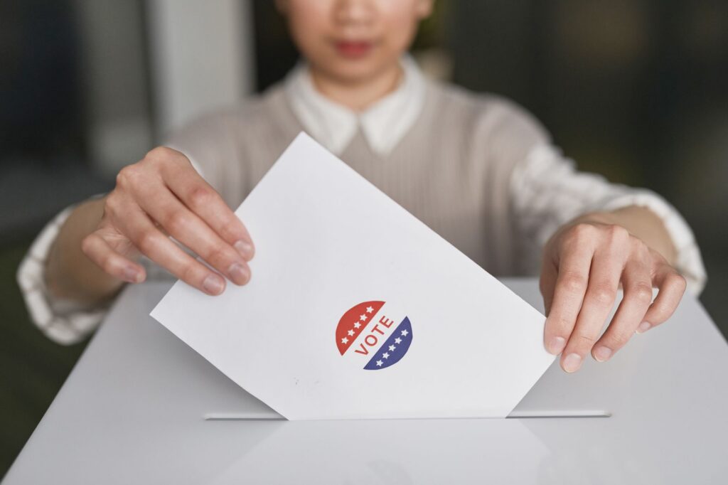 A person casting a vote by placing a ballot into a ballot box