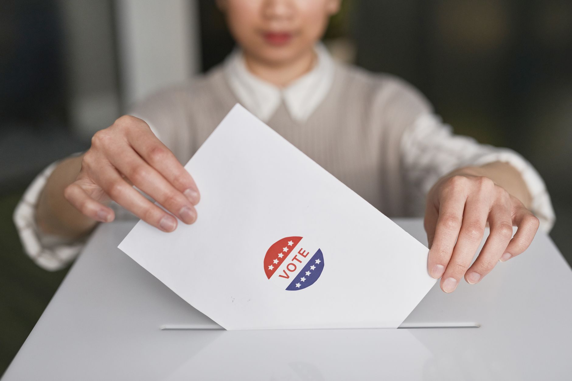 A person casting a vote by placing a ballot into a ballot box